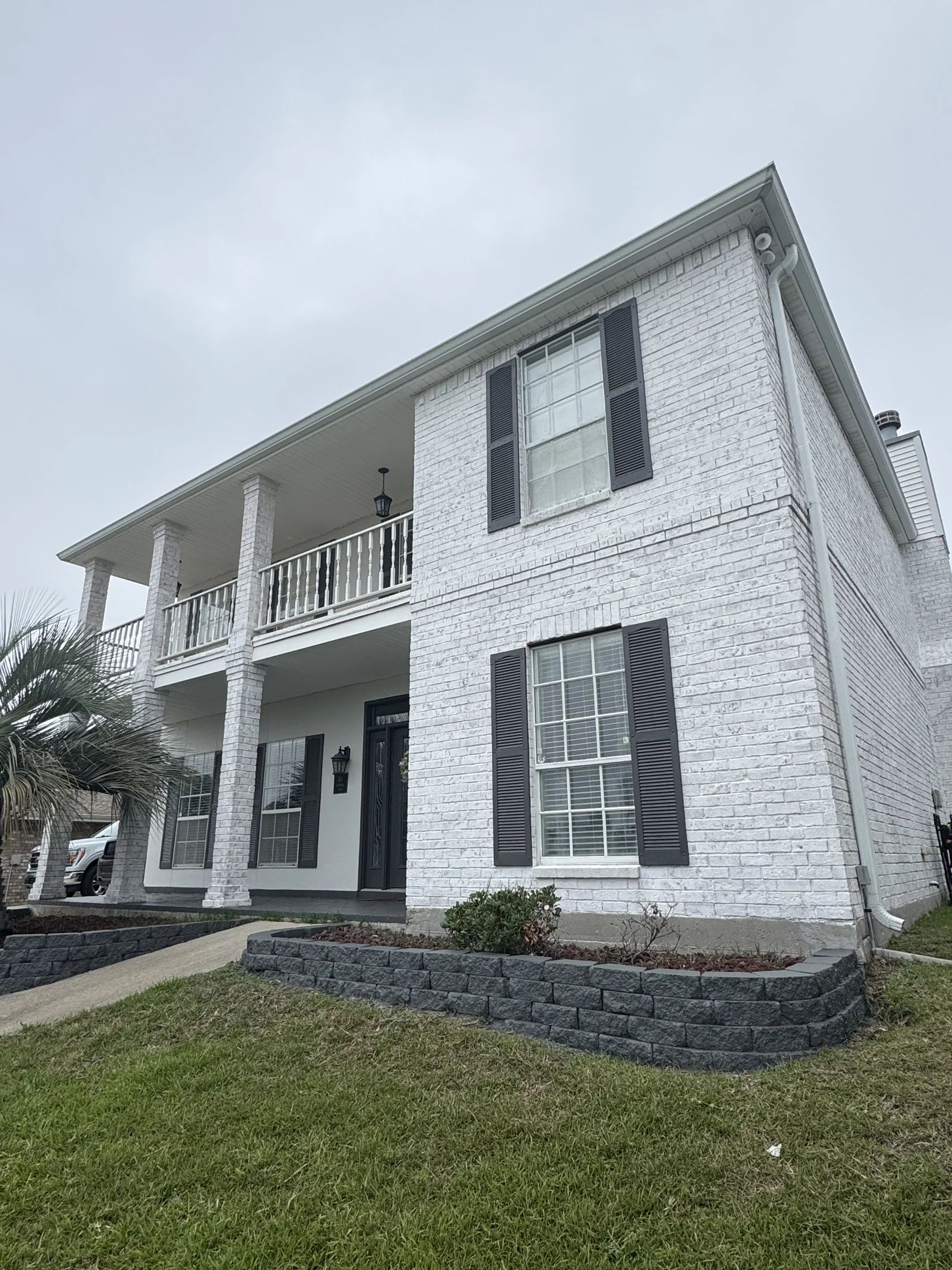 Two-story painted brick home with crisp white exterior, dark shutters, and covered upper balcony in New Orleans