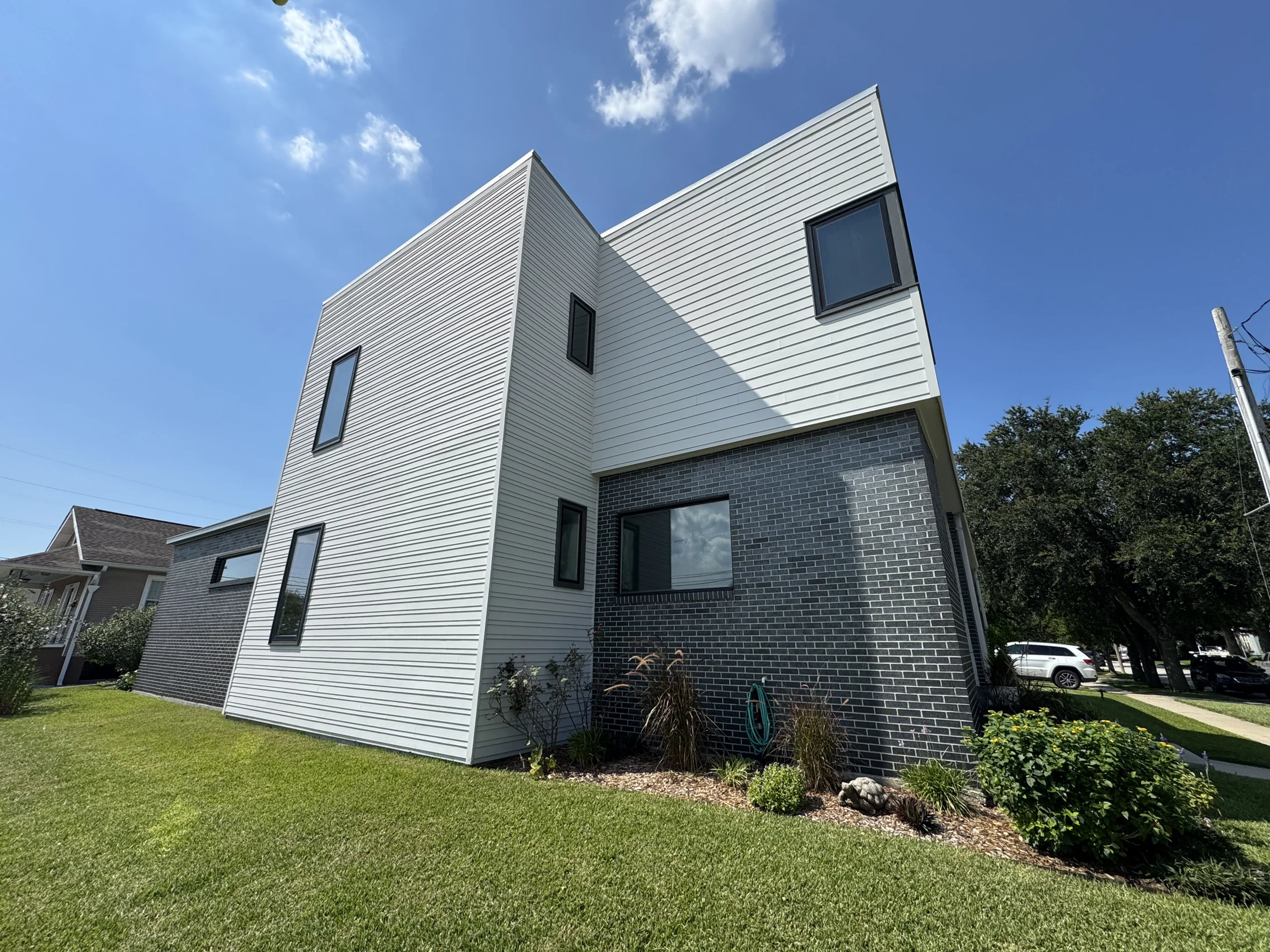 Modern two-story New Orleans home with freshly painted white horizontal siding and dark painted brick accent facade
